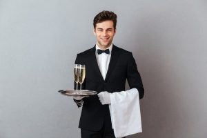 Free Photo _ Happy young waiter holding glass of champagne and towel_